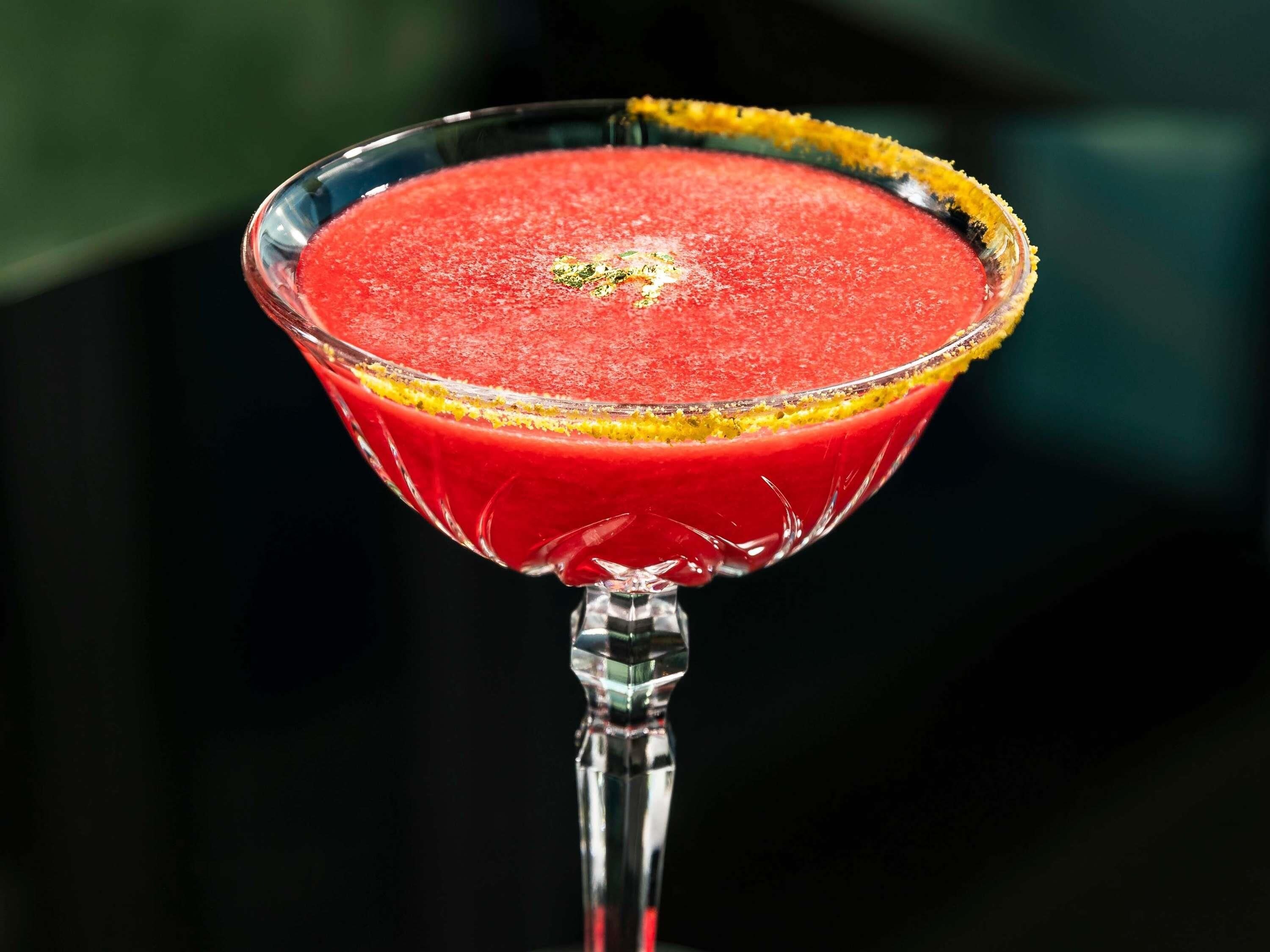 A martini glass with a red drink, garnished with a yellow rim.