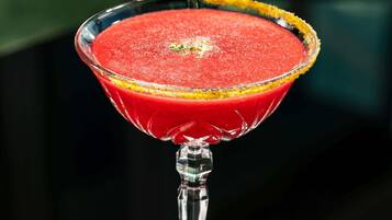 A martini glass with a red drink, garnished with a yellow rim.