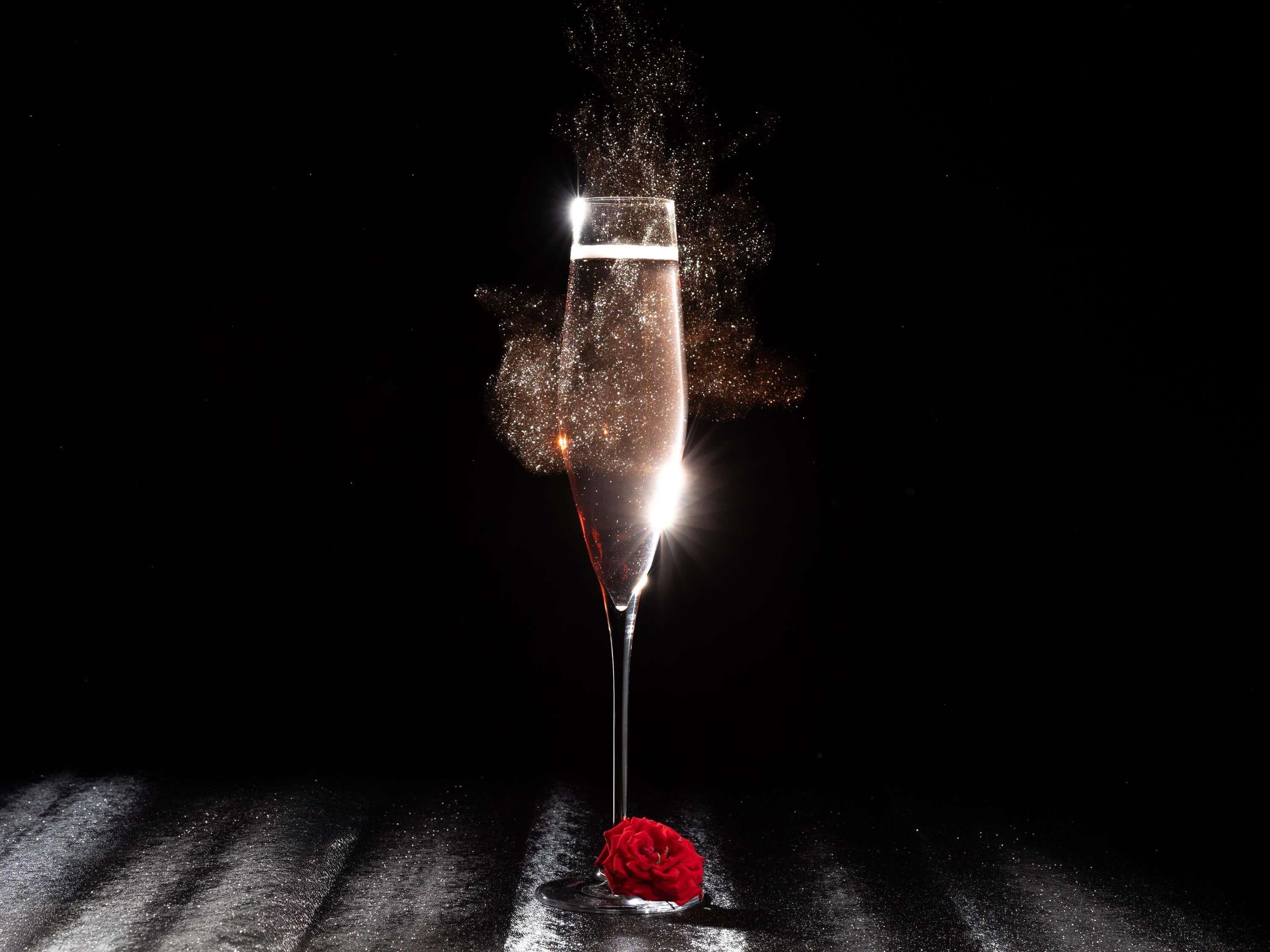 Una copa de champán con una rosa roja sobre una superficie reflectante.