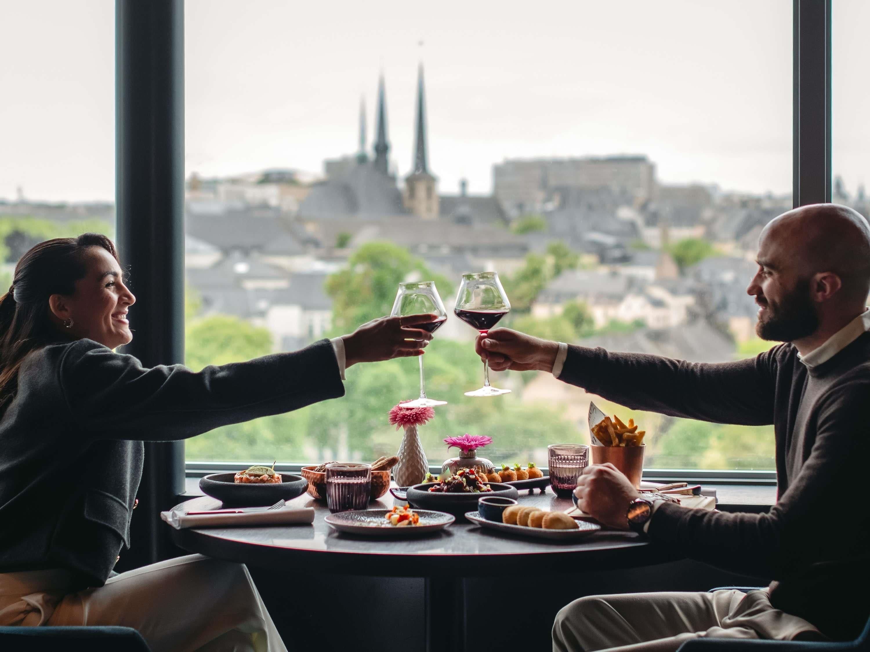 Una mesa de comedor con comida y bebidas, una ventana con vista a un paisaje urbano.