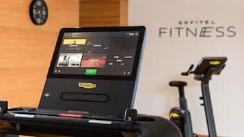 Ein Laufband mit digitaler Anzeige, die Trainingsoptionen präsentiert, und eine Wand mit dem Schriftzug "SOFITEL FITNESS".