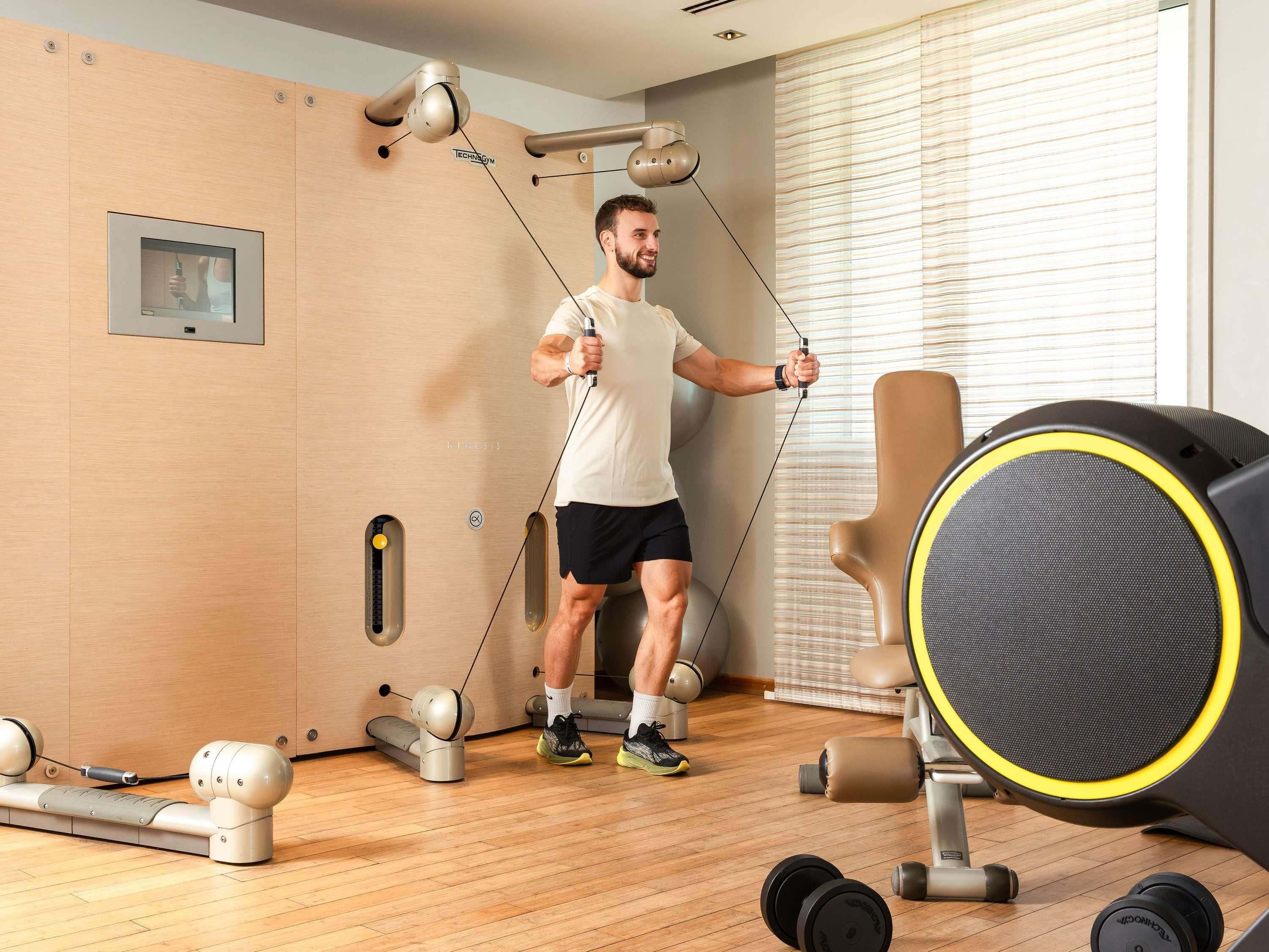 A person exercising with a resistance band in a room with a wooden floor, a punching bag, and a wall-mounted mirror.