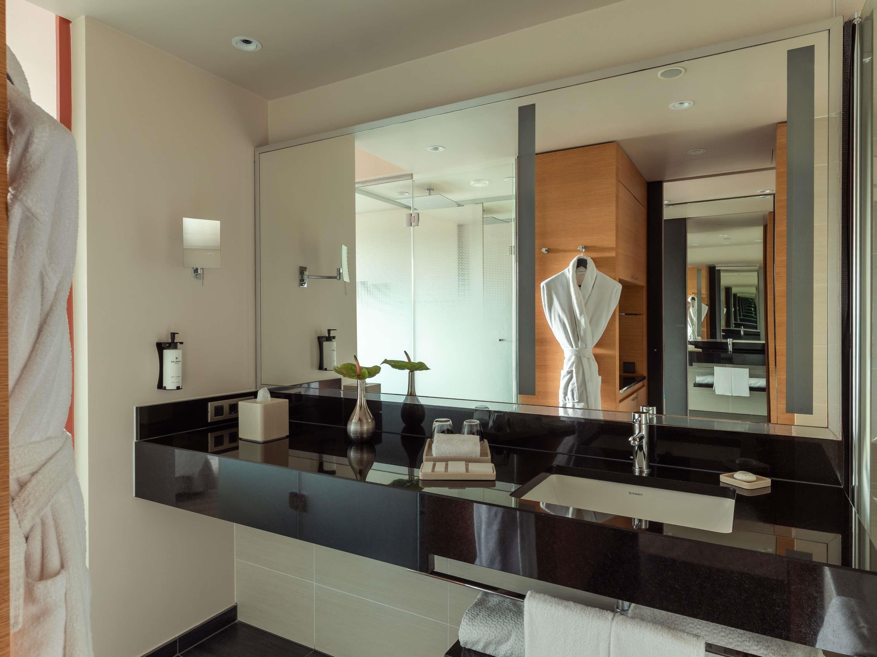Une salle de bain moderne avec un grand miroir, un peignoir suspendu et une cloison en verre.