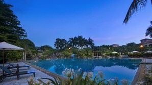 A serene pool area with lounge chairs and umbrellas, surrounded by lush greenery and palm trees. - Hillview Golf Hotel (Dongguan)