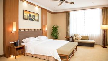 Una habitación de hotel con una cama grande, un sofá, un ventilador de techo, un cuadro en la pared y una ventana con cortinas.