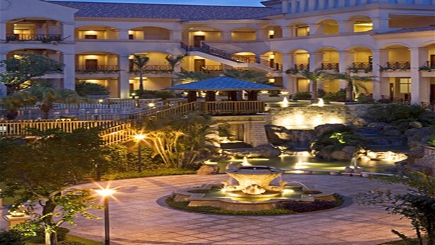 A hotel with a courtyard featuring a fountain, palm trees, and a well-lit walkway. - Hillview Golf Hotel (Dongguan)