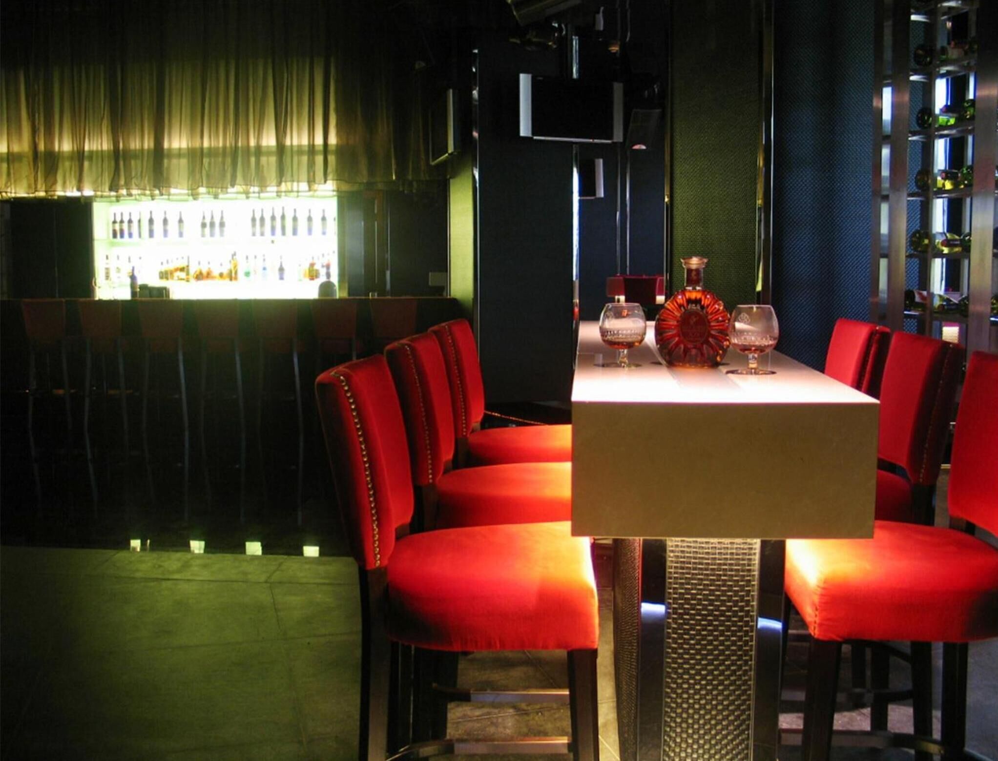 Restaurante com assentos estofados vermelhos e um bar, onde se vêem garrafas.