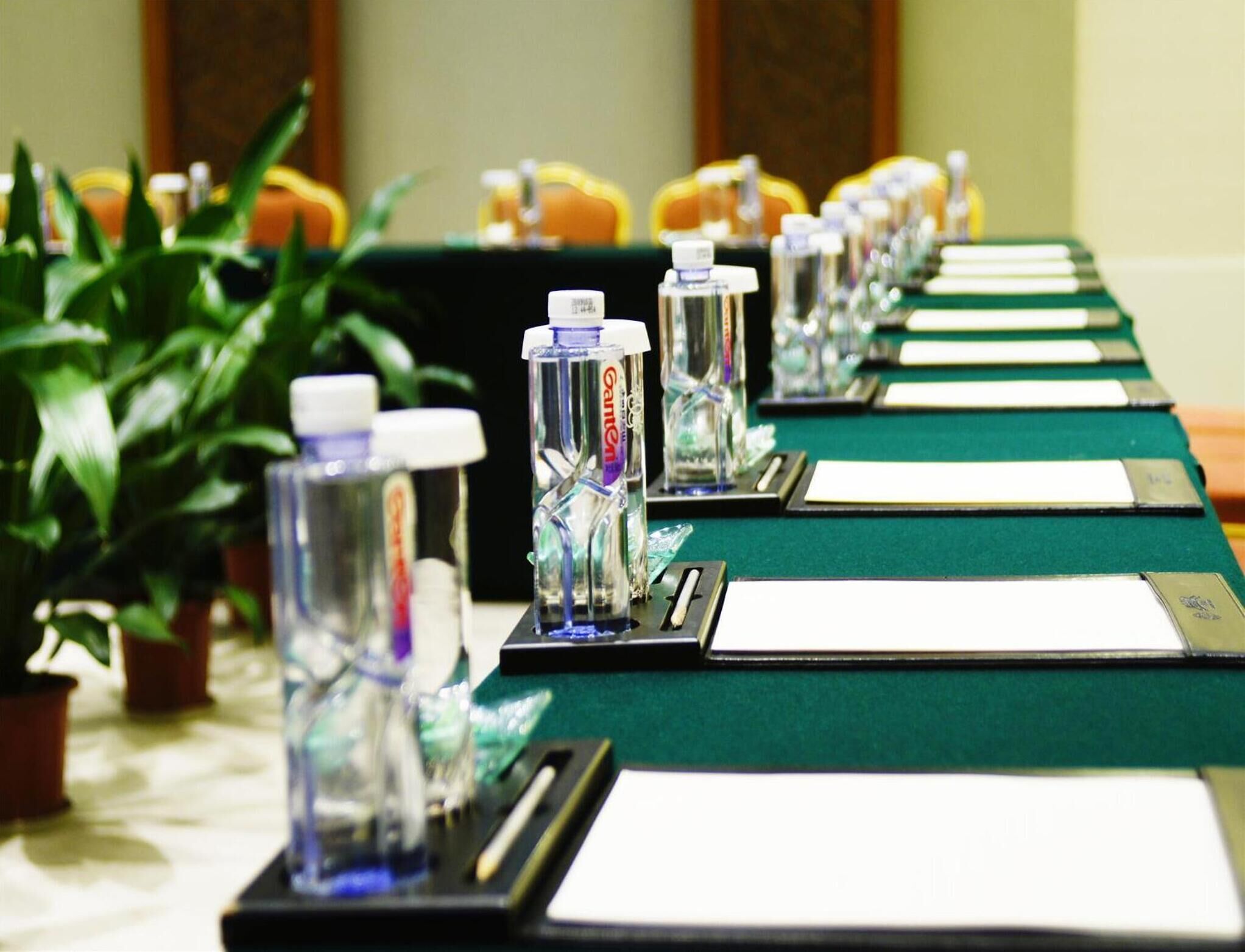 Una mesa de conferencias con botellas de agua y tarjetas de identificación, rodeada de plantas en macetas.