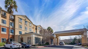 A hotel with a parking lot, a covered entrance, and a building with multiple windows and balconies.