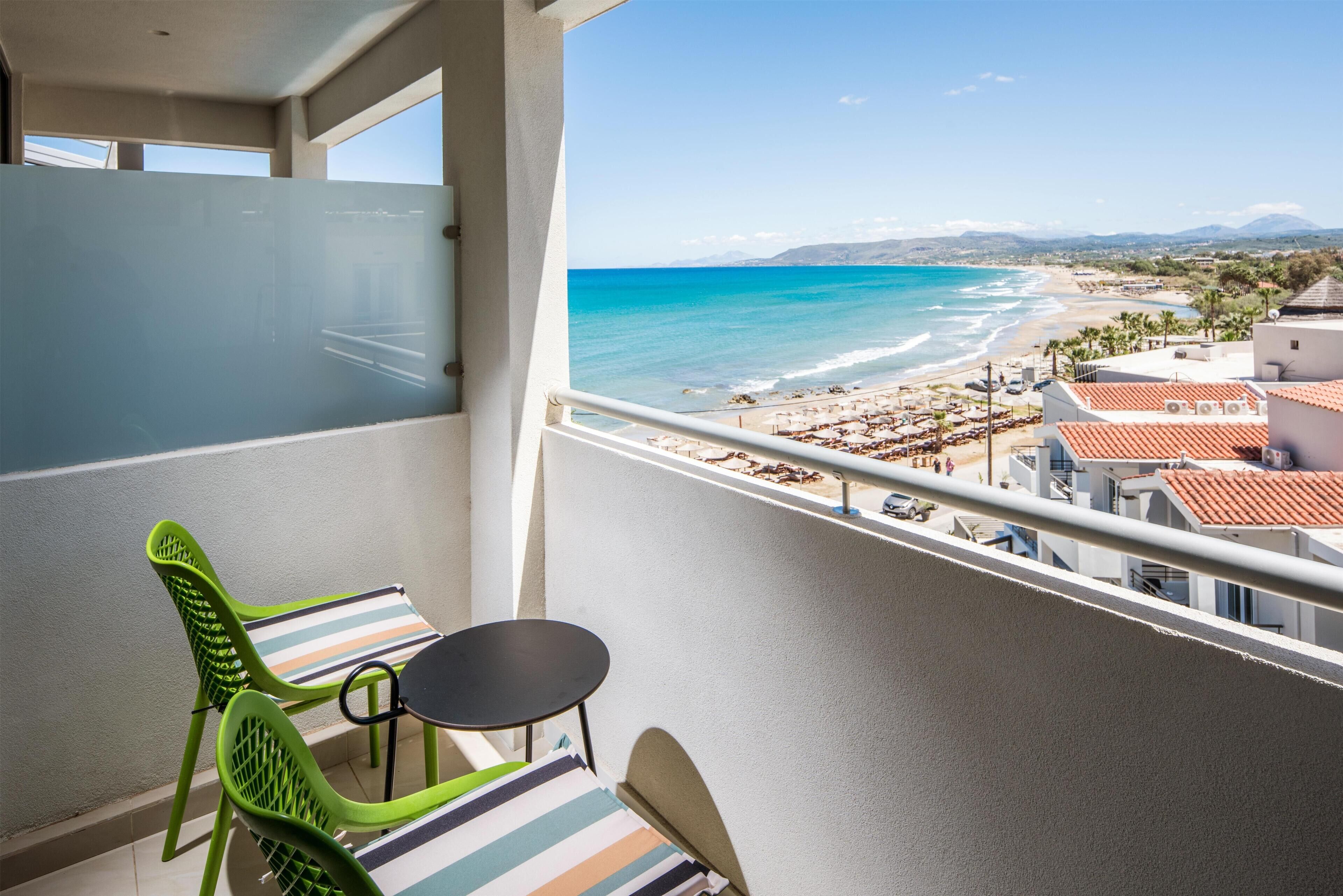 A balcony with a view of a beach, a striped chair, and a small table.