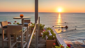 A balcony with wicker chairs, a small table, and potted plants overlooking the ocean at sunset. - Corissia Princess Hotel (Apokoronas)