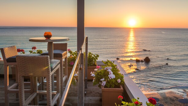A balcony with wicker chairs, a small table, and potted plants overlooking the ocean at sunset. - Corissia Princess Hotel (Apokoronas)