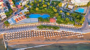 An aerial view of a resort with a large pool, beach area with sun loungers, and surrounding greenery. - Corissia Princess Hotel (Apokoronas)