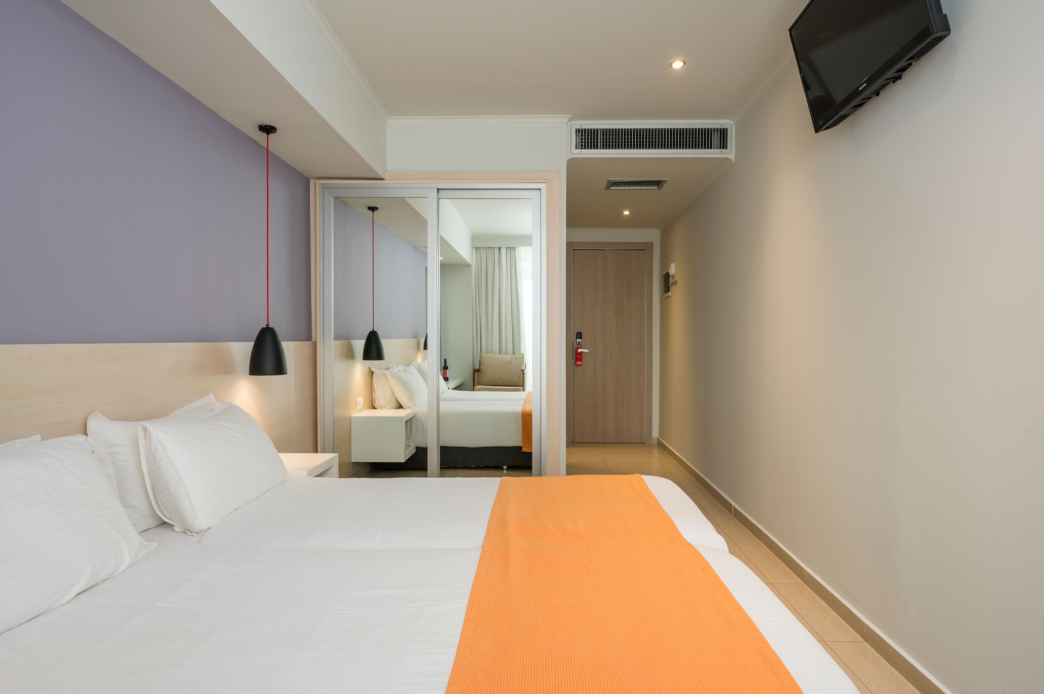 Quarto de hotel com uma cama, uma mesa de cabeceira, uma luminária, uma TV e uma porta deslizante que dá para um banheiro.