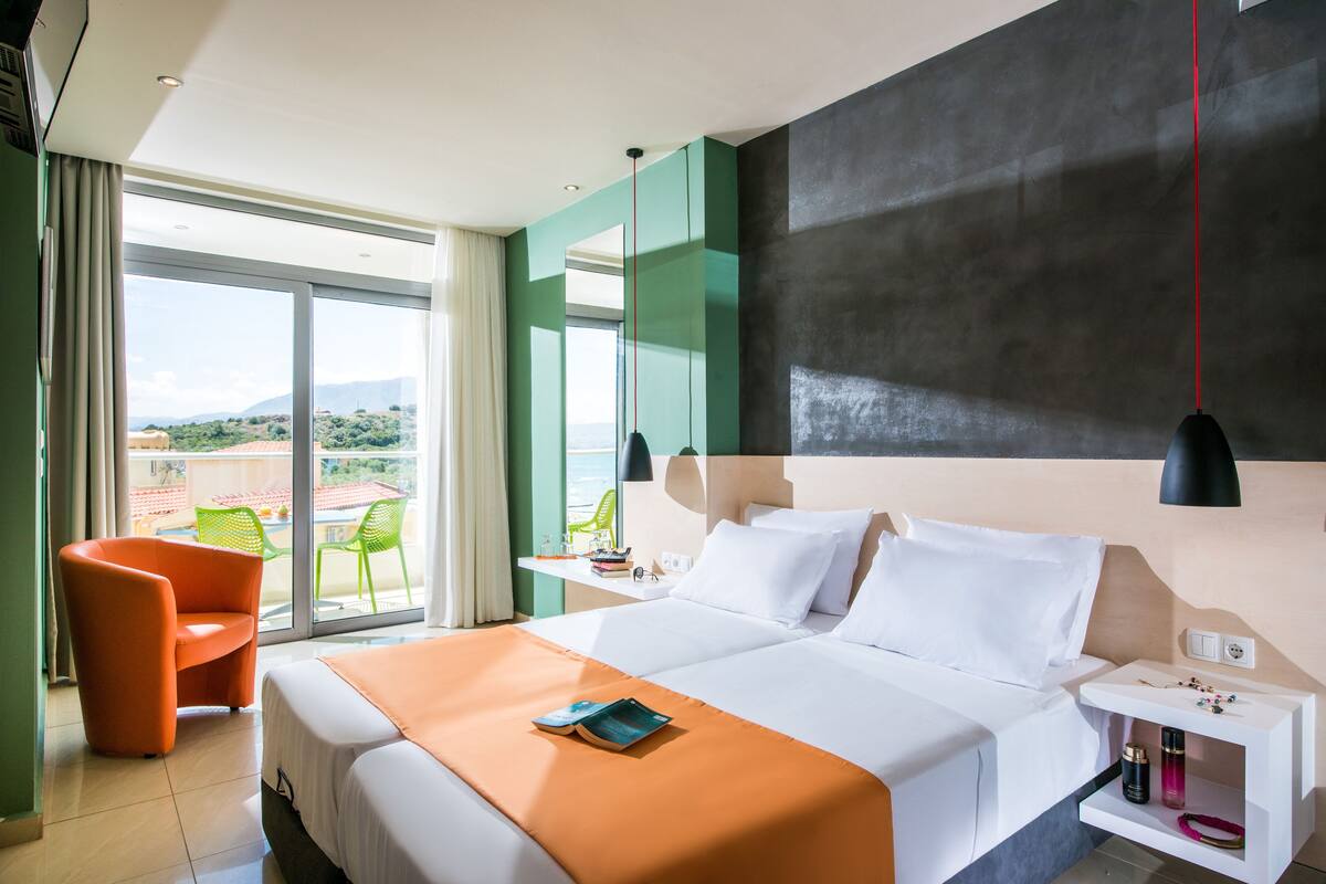 A hotel room with a large bed, a chair, a desk with a lamp, and a view of the outdoors.