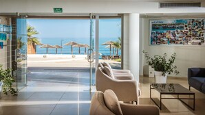 A hotel lobby with a glass door leading to a beach view, a 'wall of fame' with photos, and a seating area with a plant. - Corissia Princess Hotel (Apokoronas)
