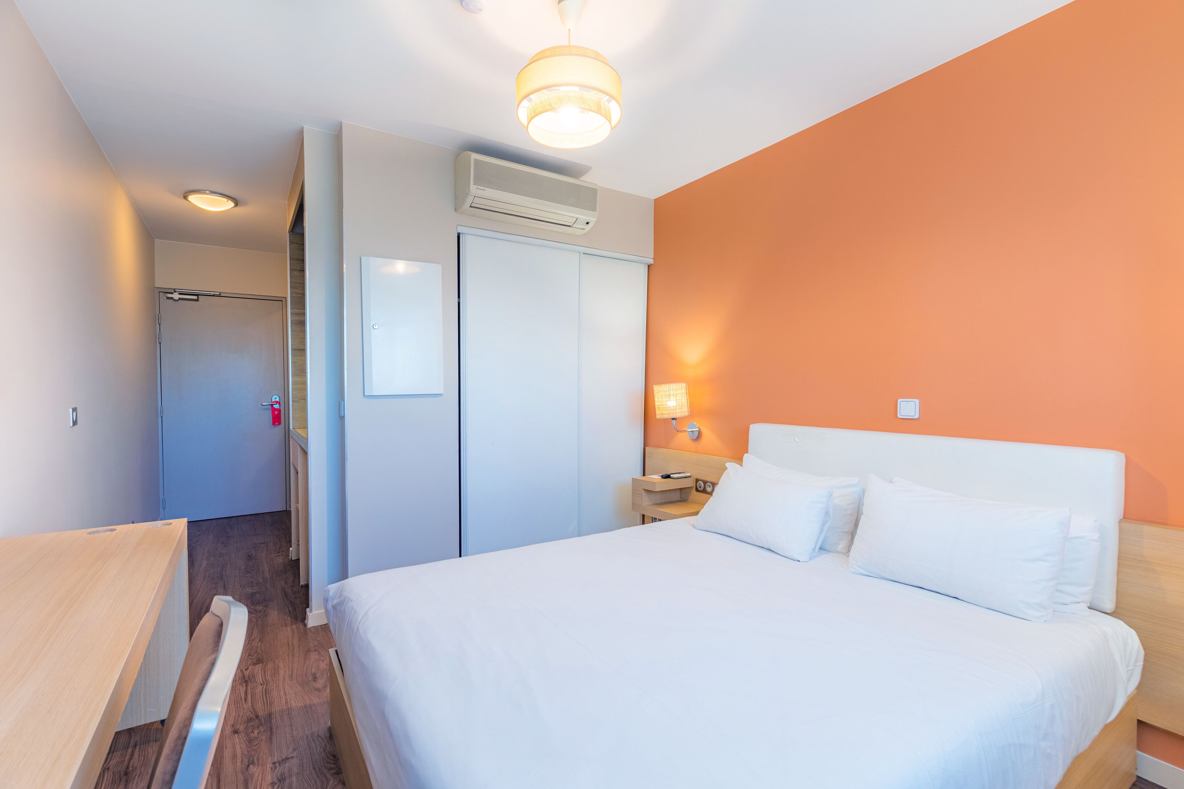 Habitación de hotel con cama, mesita de noche, aire acondicionado de pared y puerta que da a otra habitación.