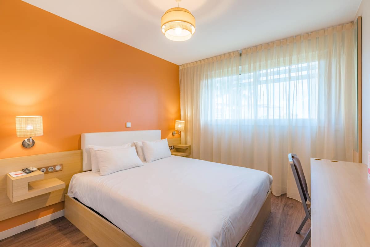 Una habitación de hotel con una cama grande, lámparas de noche, una mesita de noche y suelo de madera.