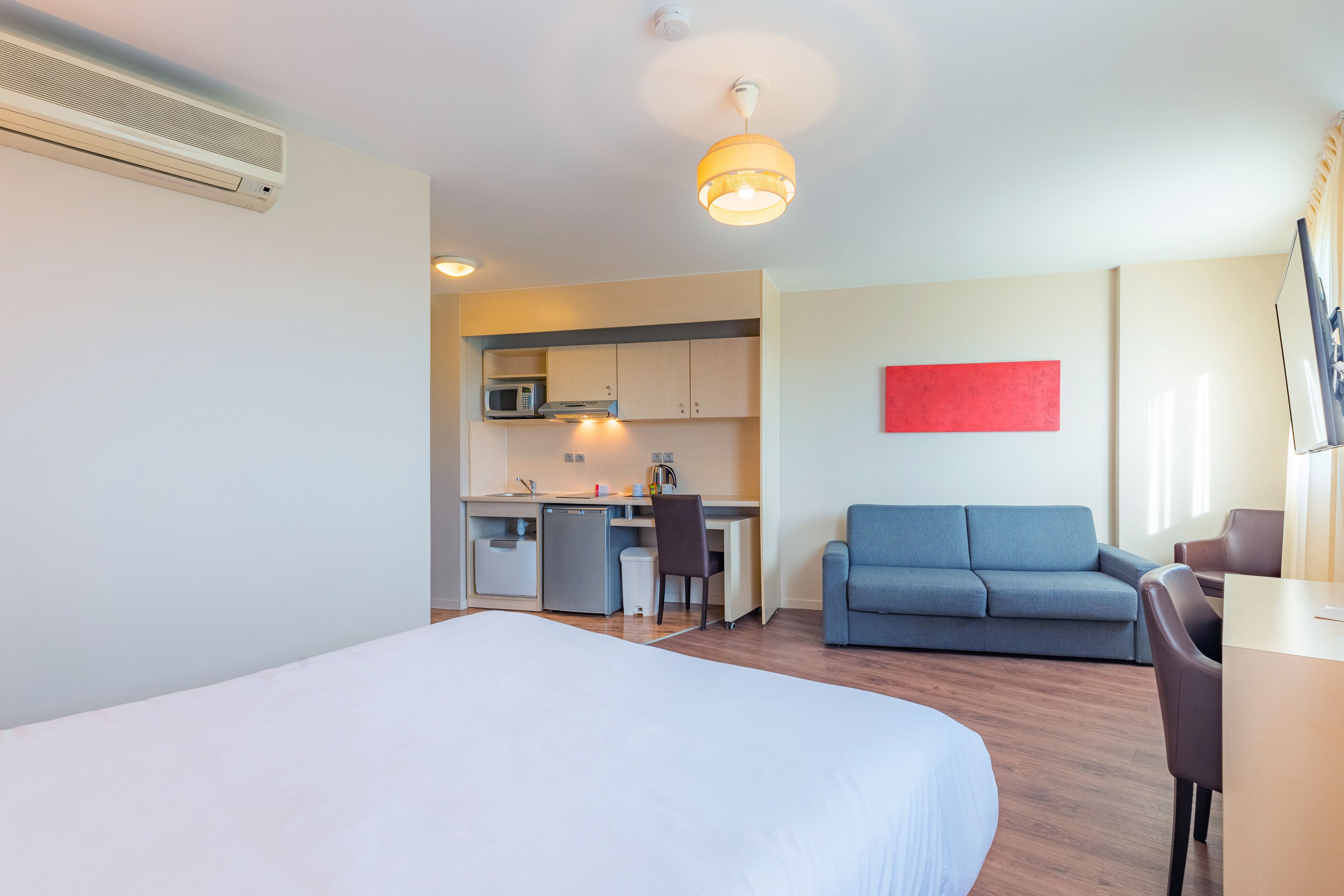 Une chambre d’hôtel avec un lit, un bureau, une kitchenette et un canapé bleu.