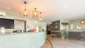A reception area with a curved counter, pendant lighting, a clock, and a potted plant. - Appart'City Confort Montpellier Ovalie 1 (Montpellier)