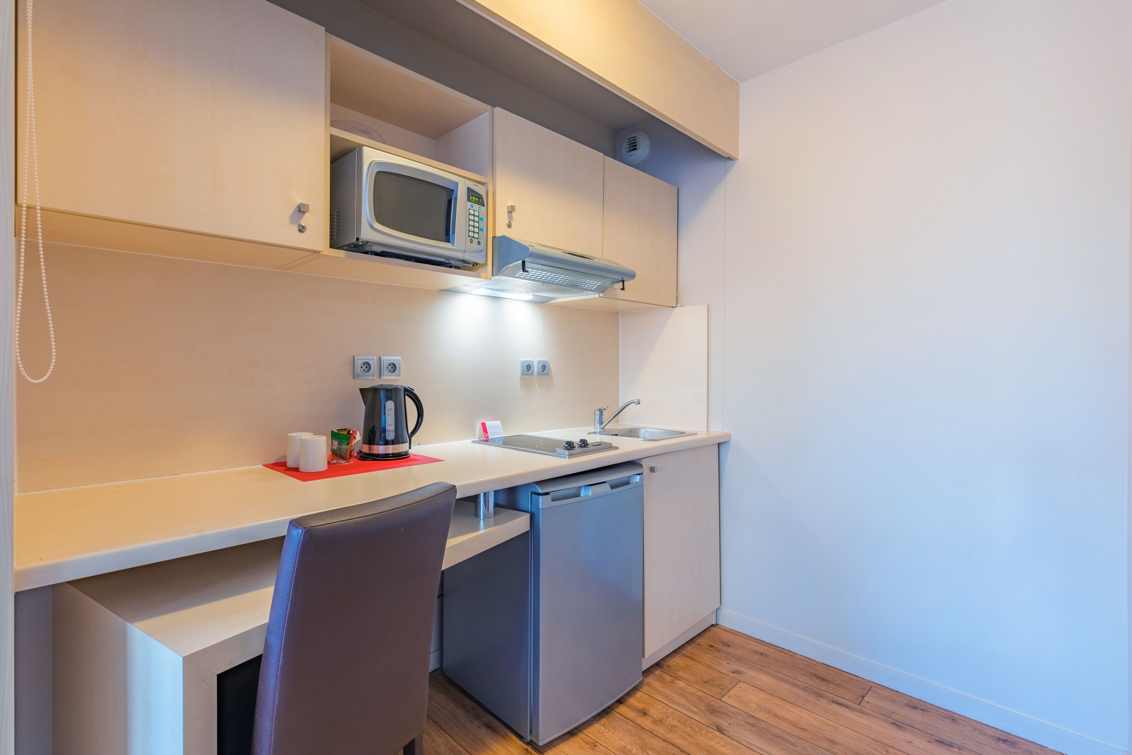 A compact kitchenette with a microwave, kettle, and sink.