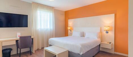 A hotel room with a bed, desk, chair, and a TV.