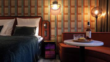 Een hotelkamer met een bed, een klein tafeltje met een fles en glazen, en een muur met een ruitpatroon.