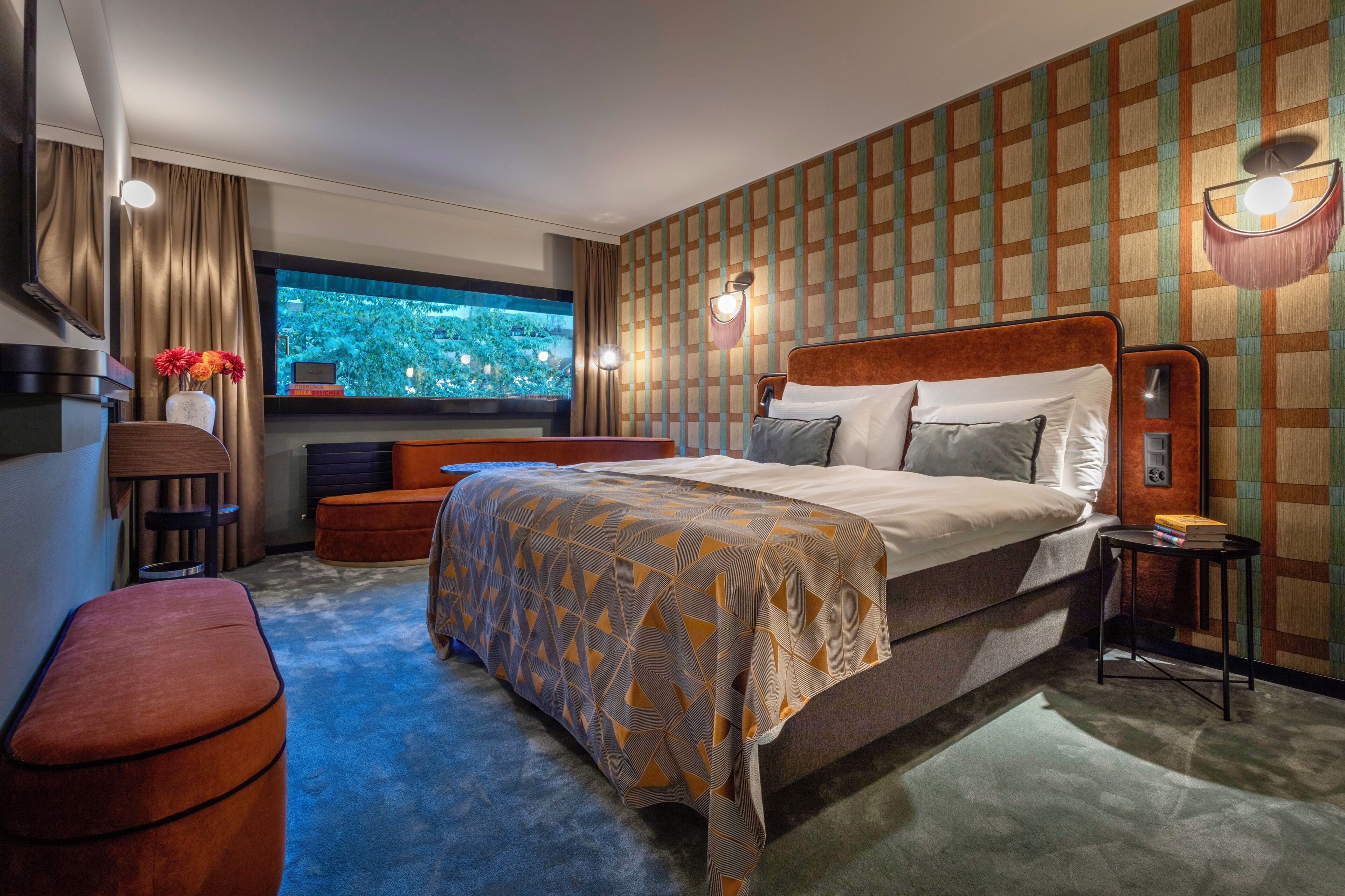 A hotel room with a large bed, a desk, a chair, a small table, and a TV.