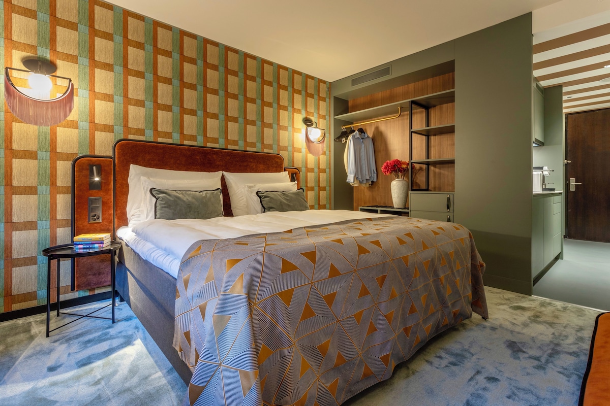 A hotel room with a large bed, a bedside table, a wardrobe, and a wall-mounted light fixture.