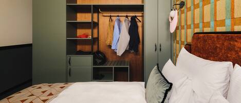 Une chambre d’hôtel avec un lit, une armoire où sont suspendus des vêtements et un mur décoré d’un motif.