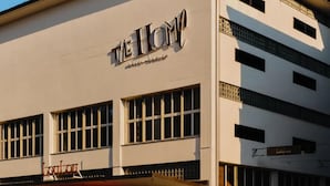Hotelli nimeltä ”The Home”, jossa on moderni julkisivu, suuret ikkunat ja ulkona oleva oleskelualue, jossa on aurinkovarjoja.
