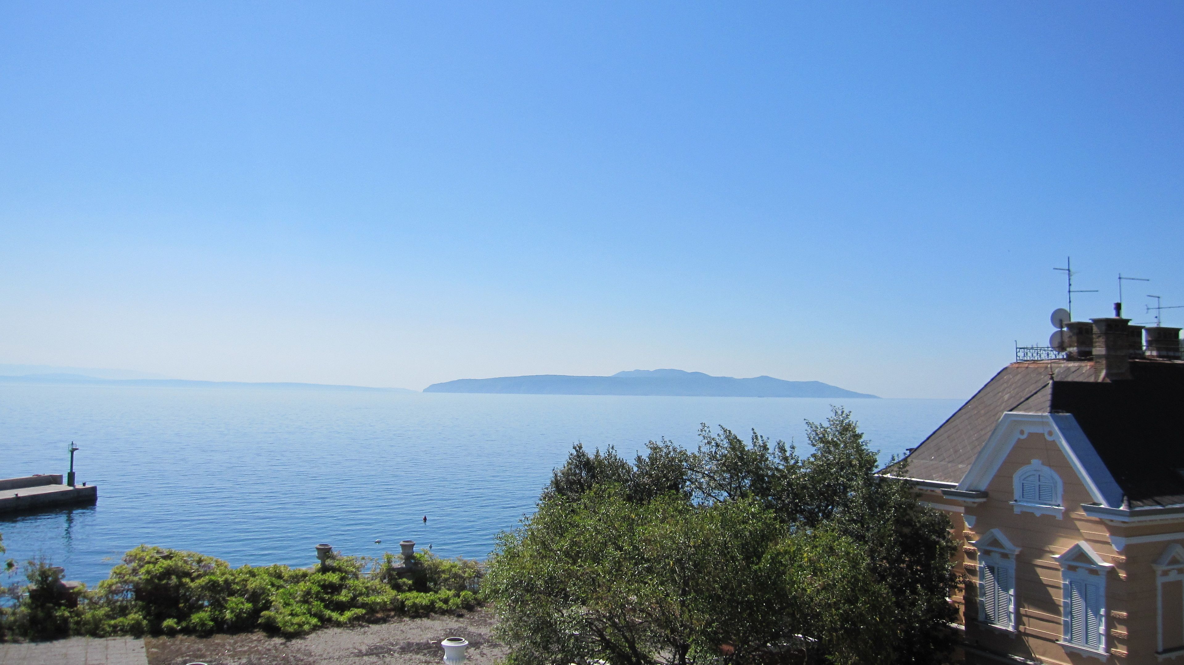 Paesaggio costiero con cielo sereno, mare calmo, terraferma in lontananza e un edificio in stile architettonico tradizionale.