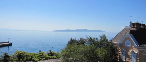 A coastal view with a clear sky, calm sea, distant landmass, and a building with a traditional architectural style.