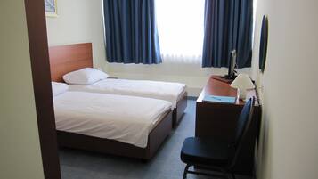 A hotel room with two single beds, a desk with a lamp, a chair, and a window with curtains.