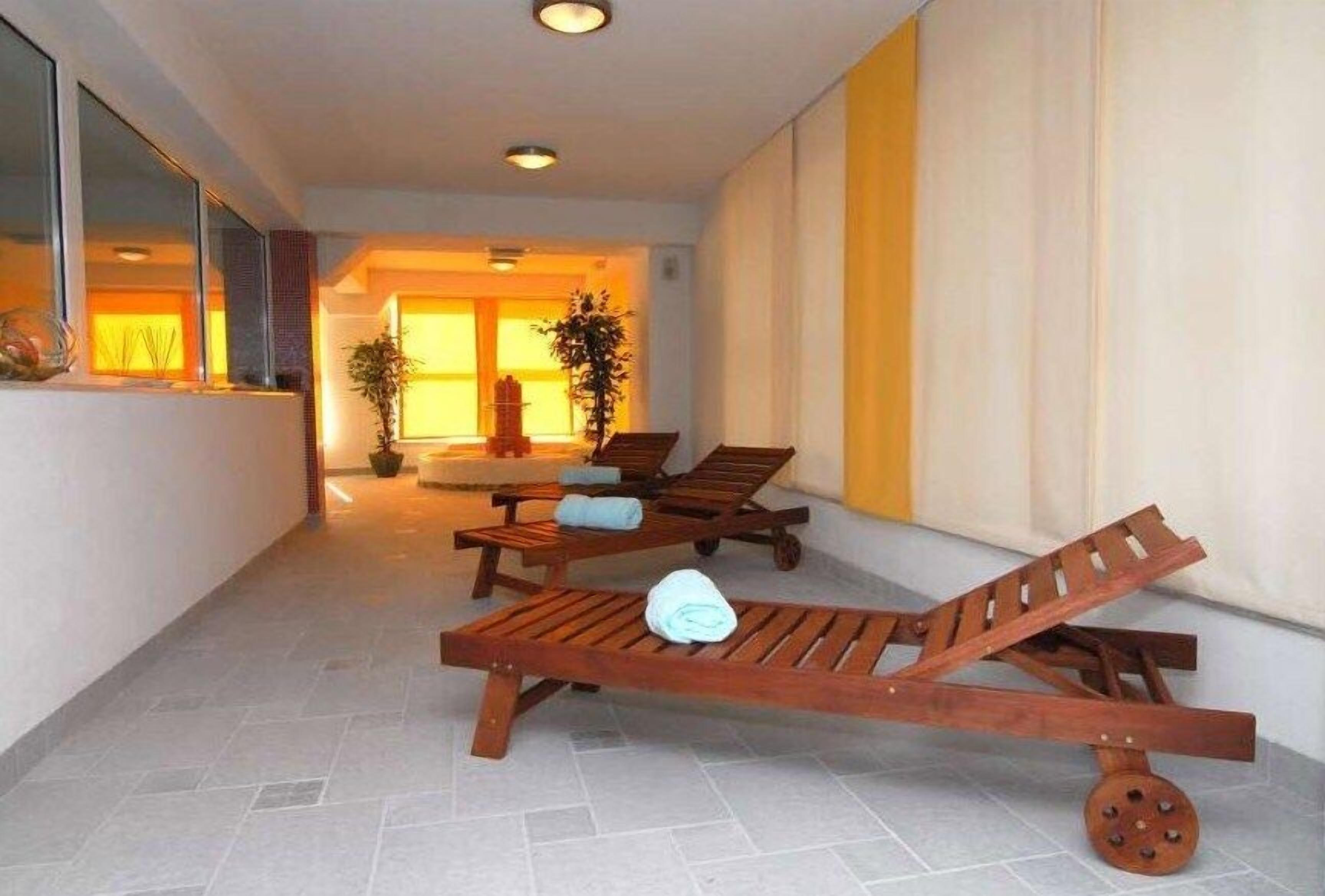 Un pasillo con sillones de madera, una planta en maceta y vistas a una habitación con un ventanal grande.