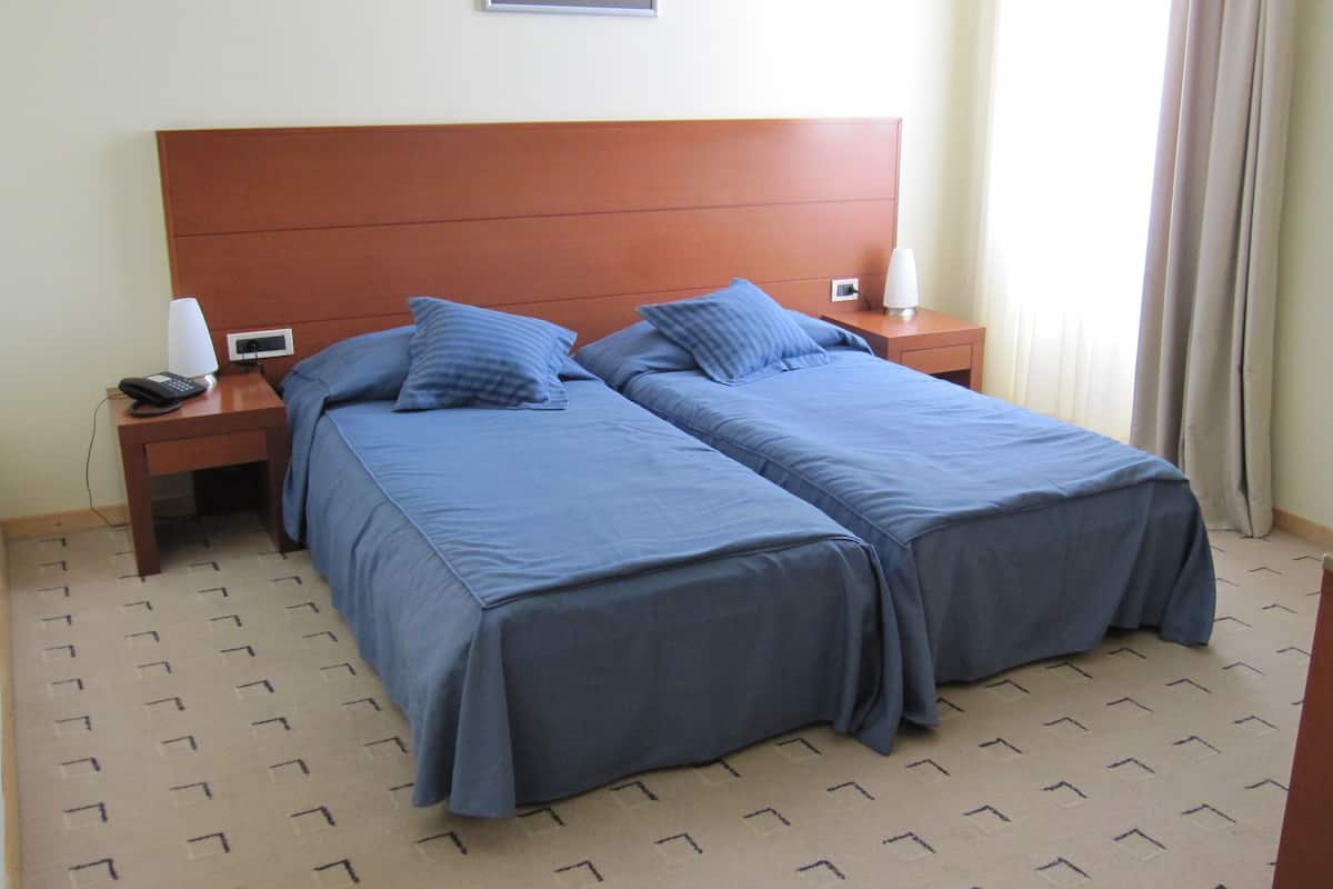 A hotel room with two beds, a wooden headboard, a bedside table with a lamp, and a phone.