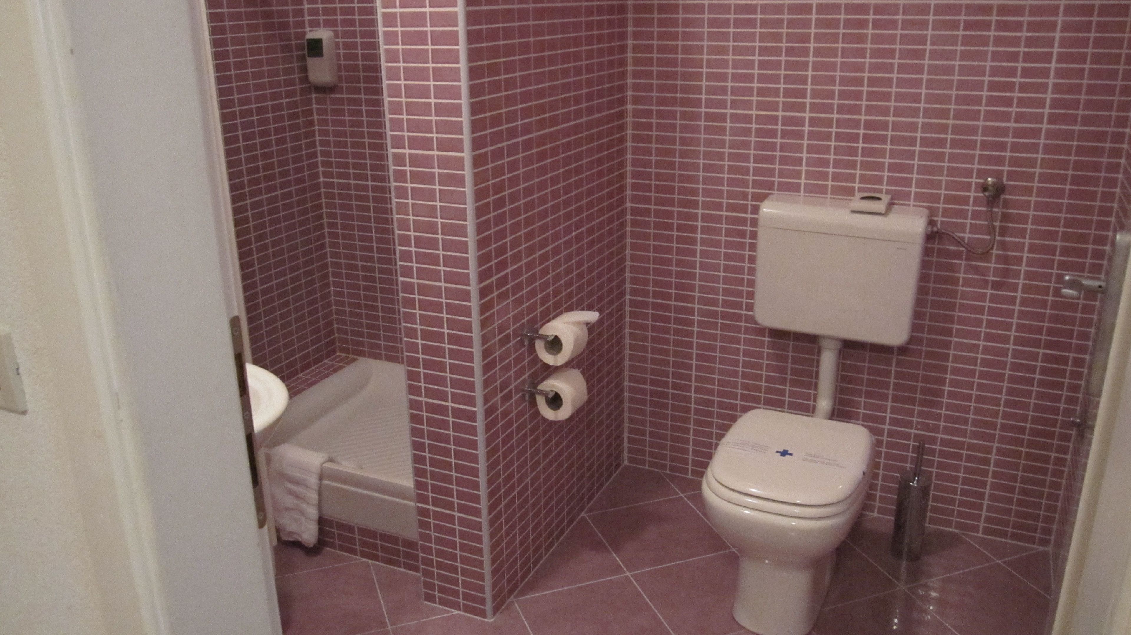 A small bathroom with a toilet, two rolls of toilet paper, and a soap dispenser on the wall.