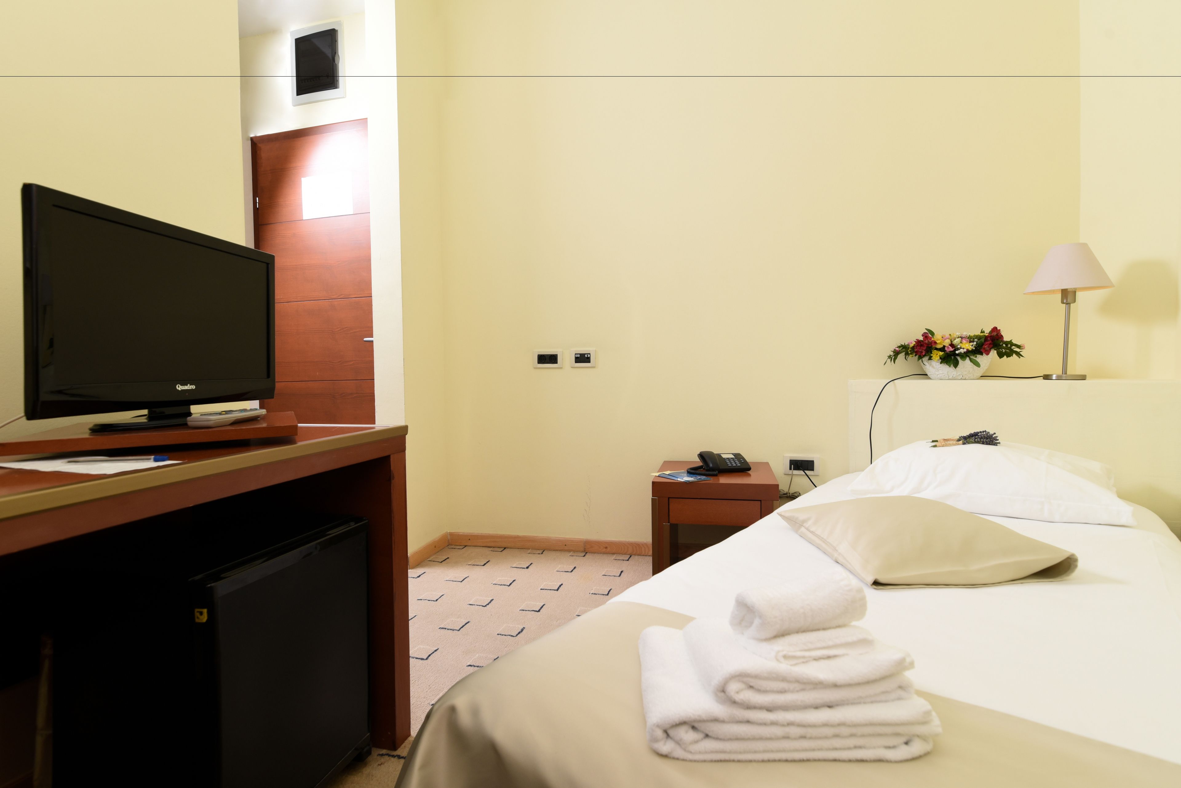Ein Hotelzimmer mit einem Bett, einem Schreibtisch mit Fernseher, einem kleinen Tisch mit Lampe und einem an der Wand befestigten Telefon.