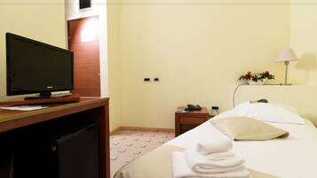 Ein Hotelzimmer mit einem Bett, einem Schreibtisch mit Fernseher, einem kleinen Tisch mit Lampe und einem an der Wand befestigten Telefon.