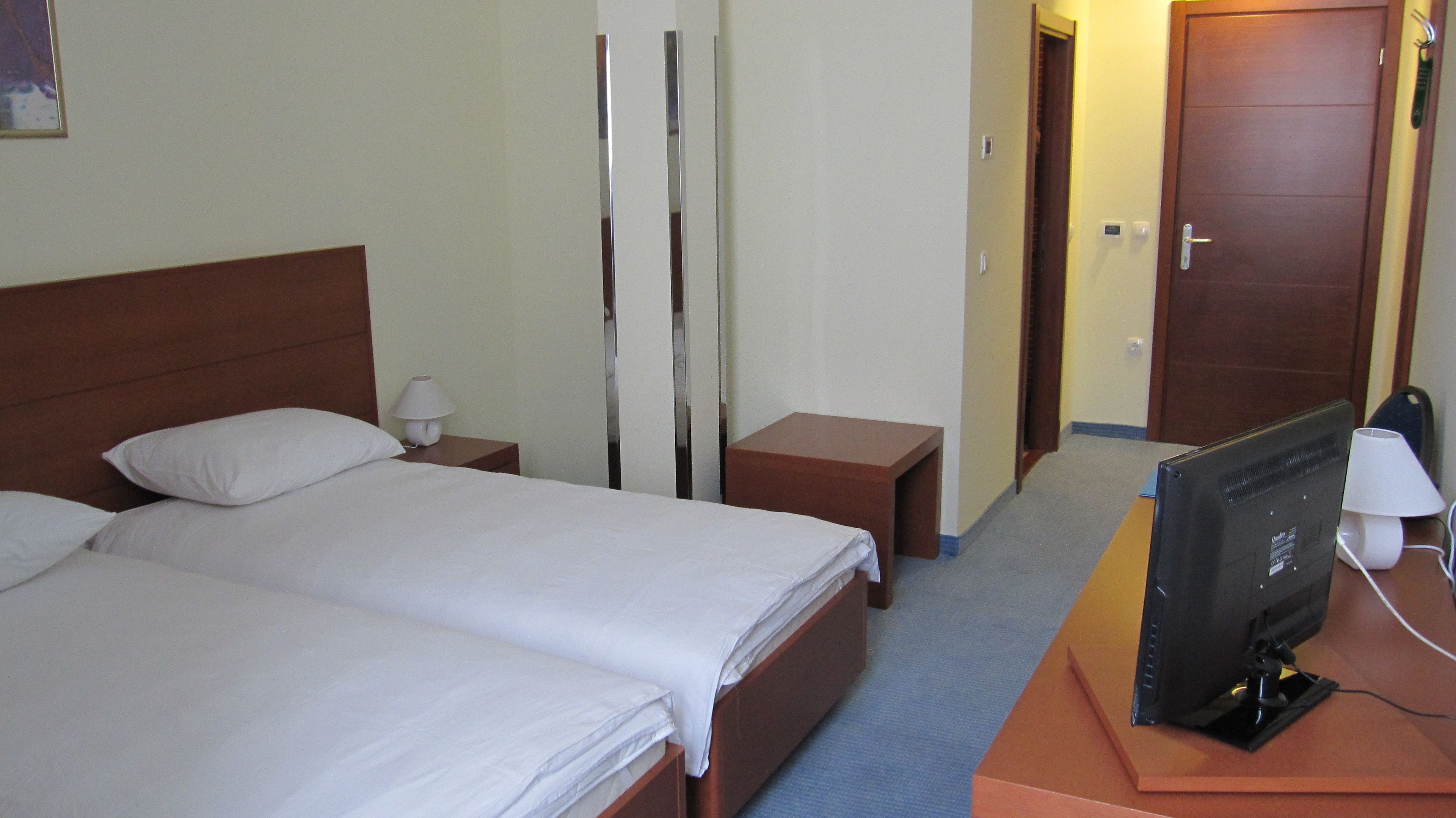 A hotel room with two beds, a TV, a bedside table, and a lamp.