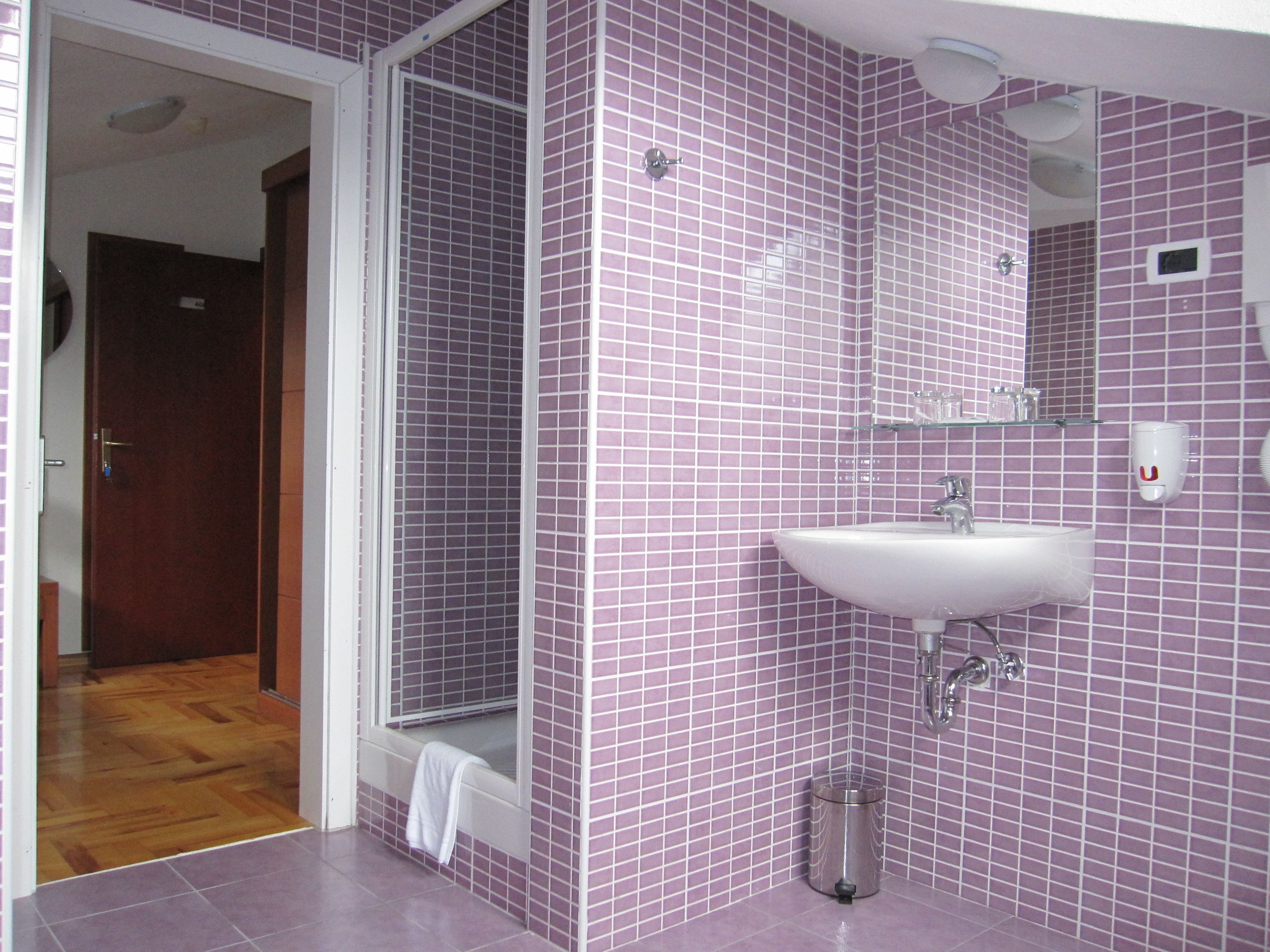 A bathroom with purple tiled walls, a white sink, and a glass shower enclosure.