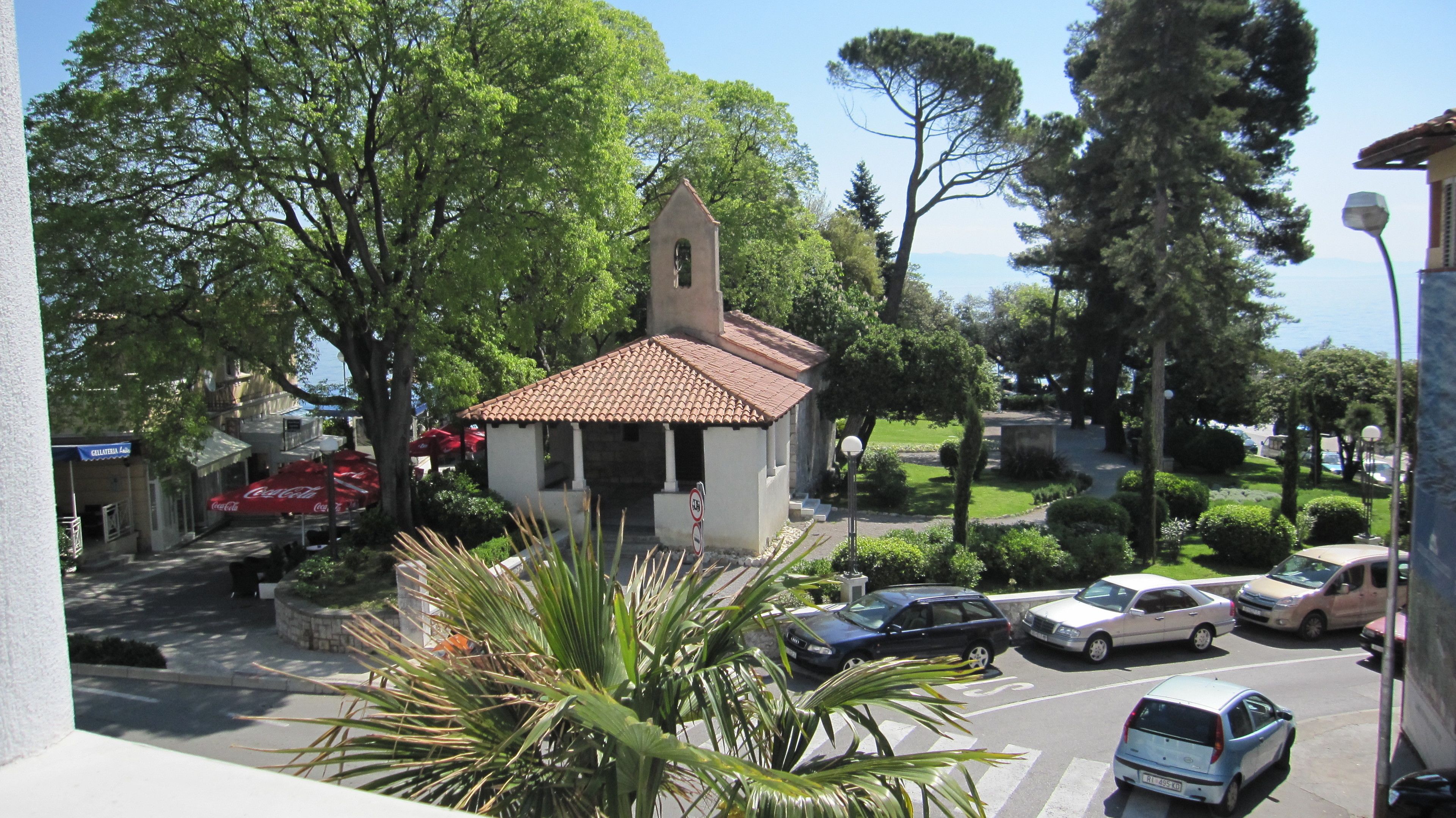 A small building with a tiled roof, surrounded by trees and parked cars.