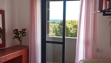 Una camera da letto con una porta vetrata scorrevole su un balcone, un comodino con un vaso di fiori e un letto con coperta verde.