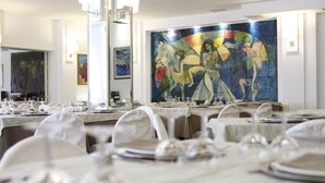 A dining area with tables set for a meal, a large abstract painting on the wall, and a chandelier above. - Hotel Califfo (Quartu Sant'Elena)