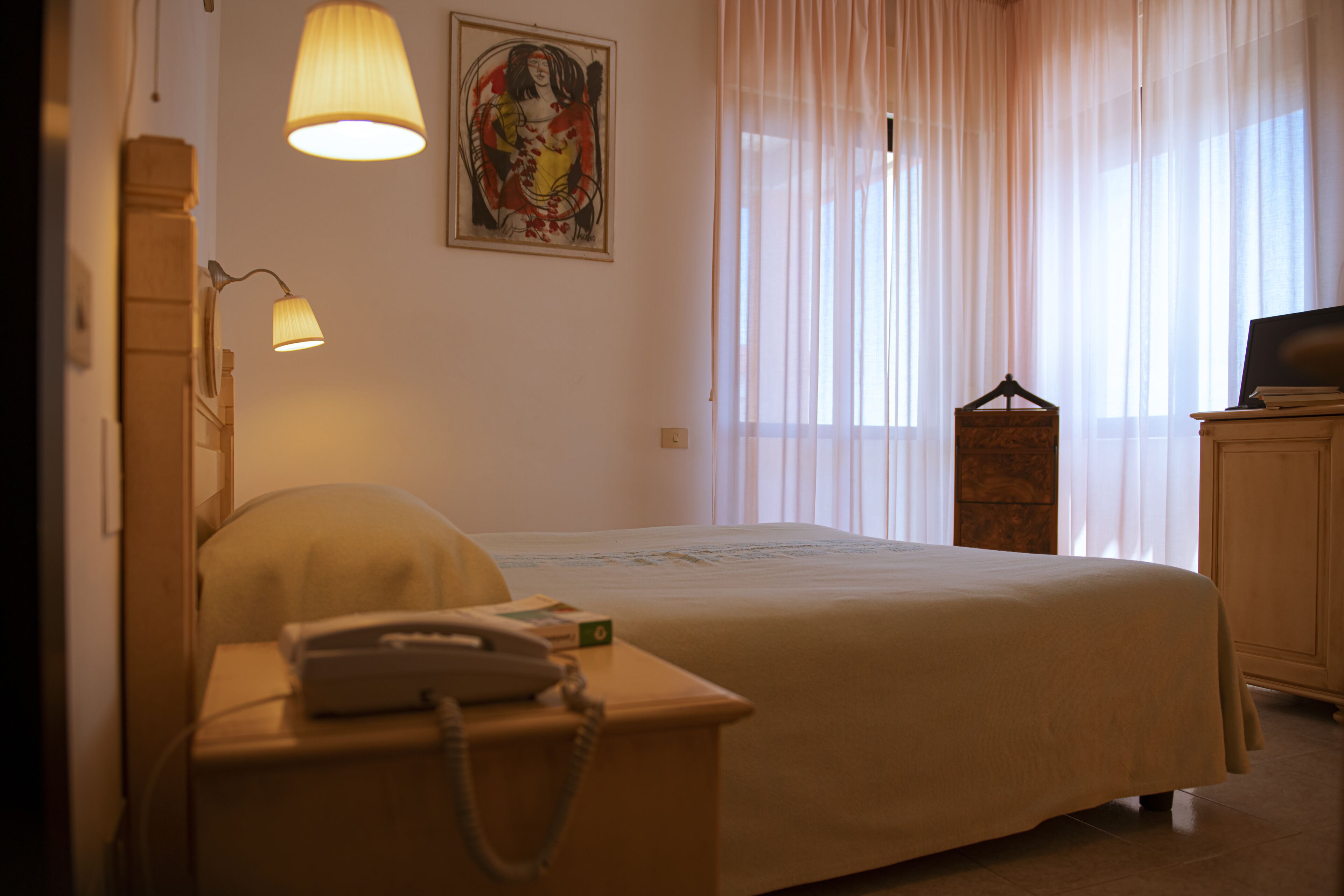 A hotel room with a bed, bedside lamp, telephone, and a television on a cabinet.