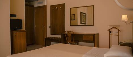 Habitación de hotel con cama, escritorio, silla, televisor, espejo y lámpara.