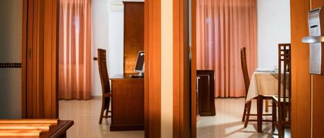 A hotel room with a wooden desk, a chair, a dining table, and a view of the living area.
