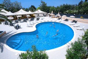 Una piscina con sillas de descanso y sombrillas, rodeada de vegetación y un cielo despejado.