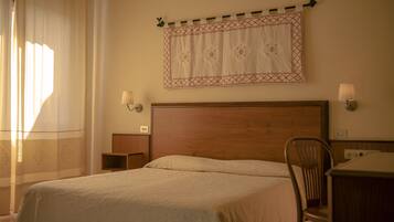 Habitación de hotel con cabecera de madera, una cama individual, una silla, un escritorio y dos lámparas fijadas a la pared.