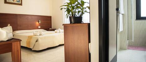 A hotel room with a bed, bedside table, and a potted plant.